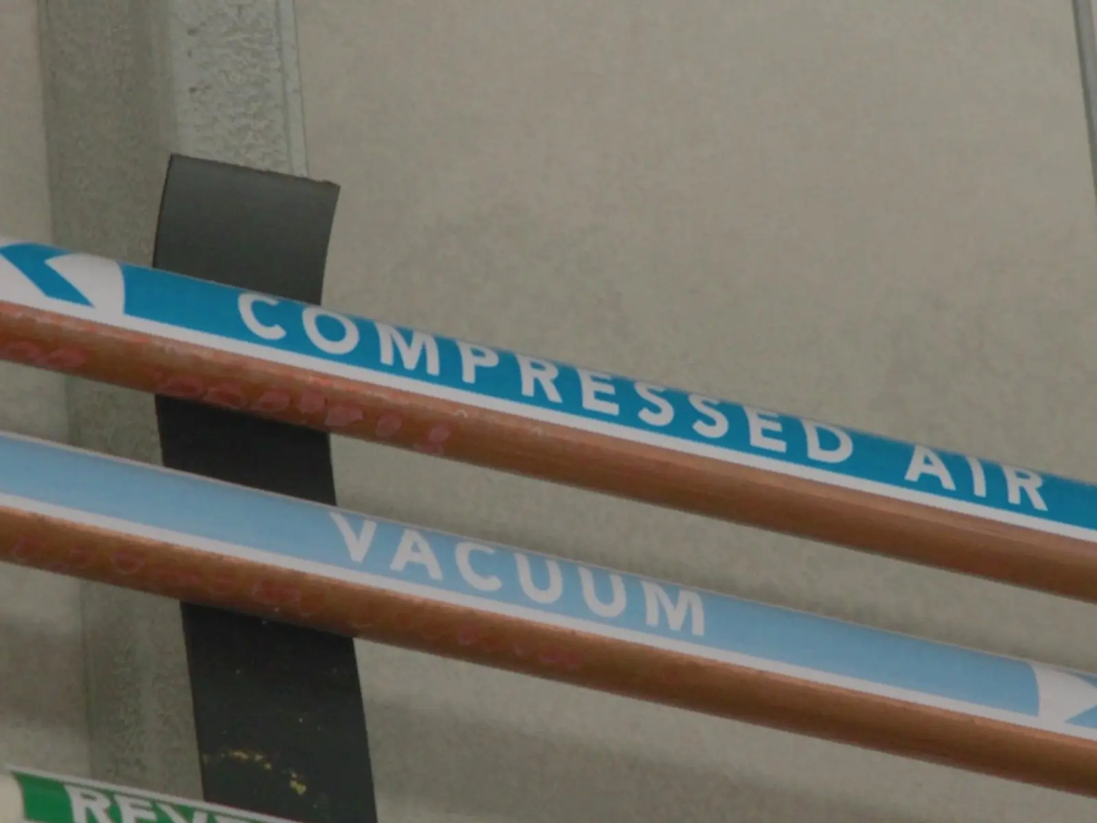 Runs of copper and steel services pipework on a commercial ceiling, each line labelled with its own identification tape reading compressed air, vacuum and reverse osmosis water