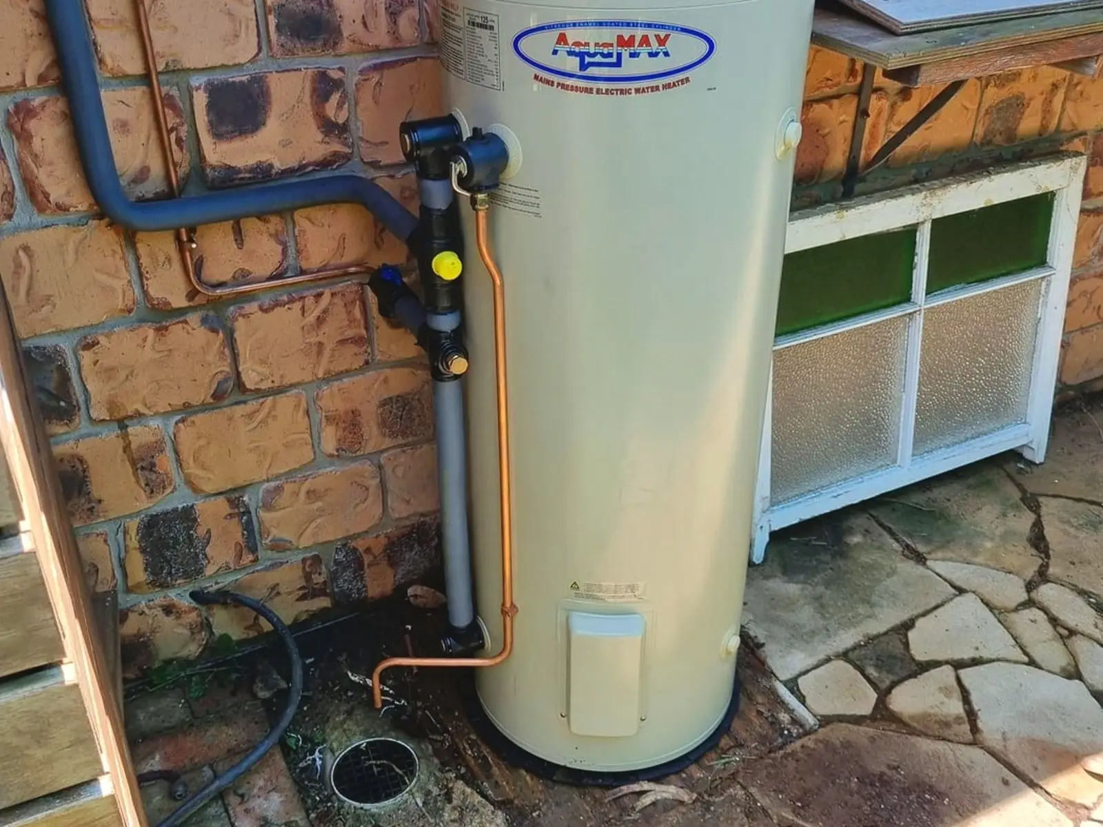 A mains pressure electric storage hot water unit installed against a brick wall with new copper pipework, a tempering valve on the outlet and lagged flow and return lines